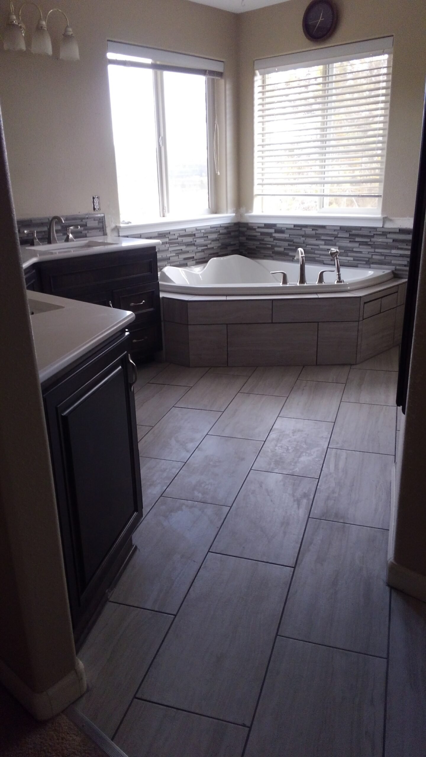 Renovated bathroom with corner bathtub, tile, and vanities